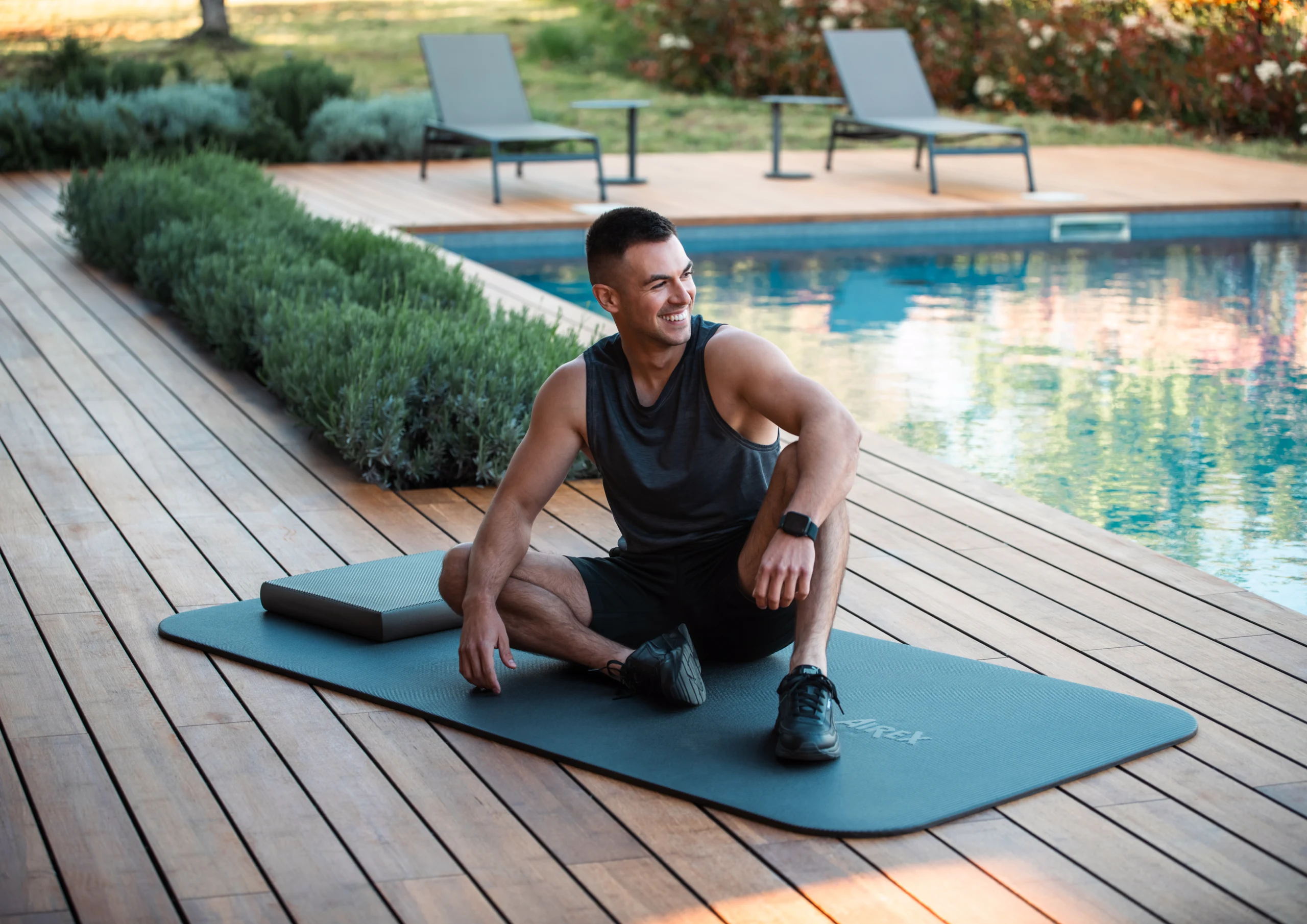 Man seated on an exercise mat beside a pool.