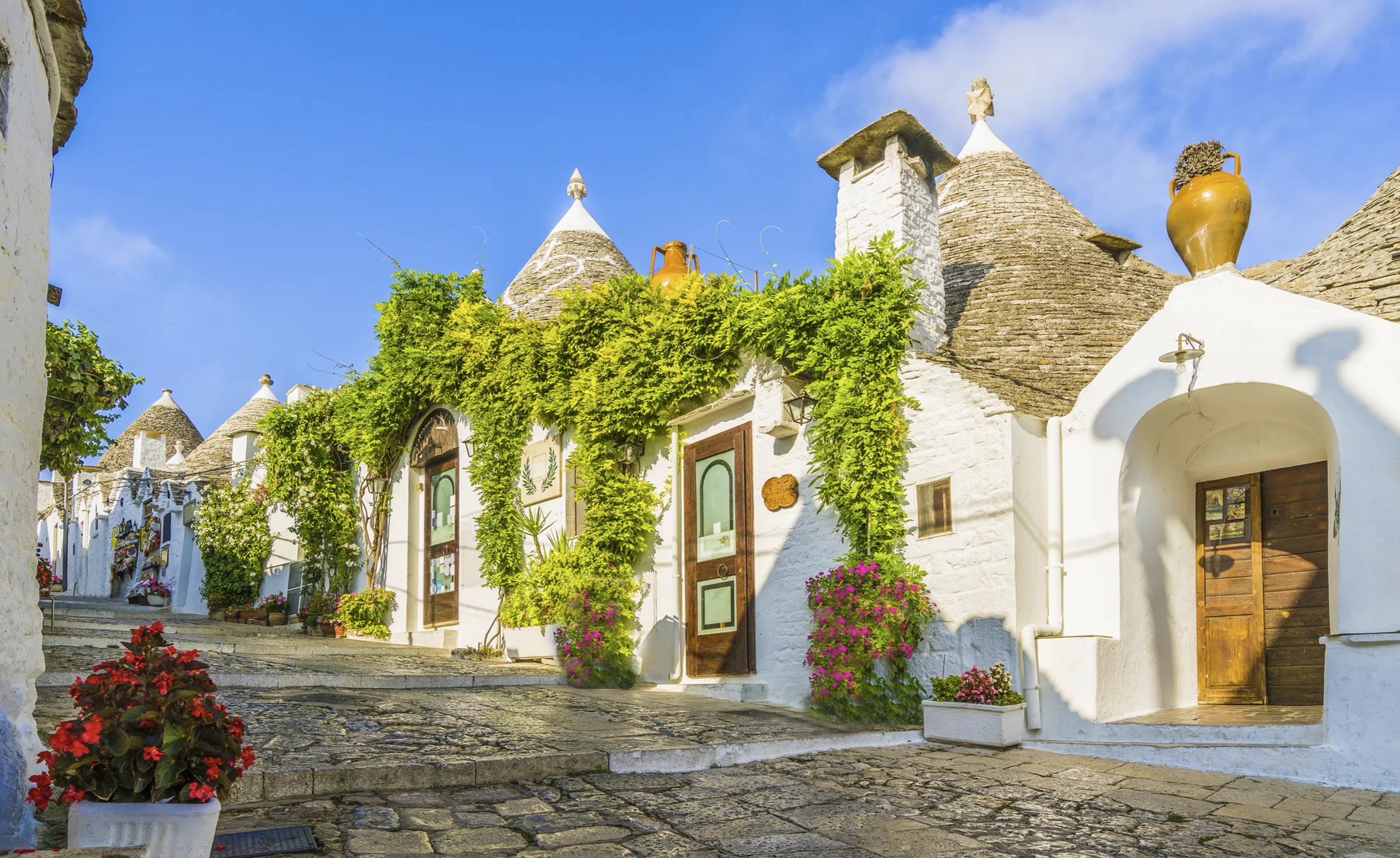 White trulli-style buildings along a stone street with greenery
