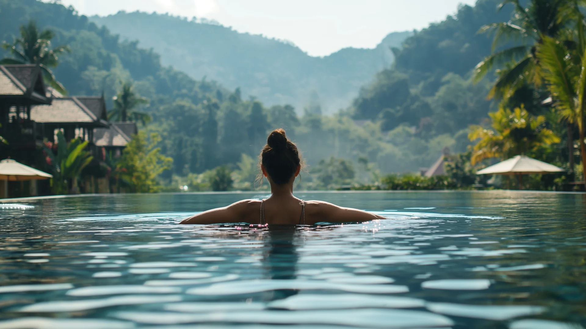 Woman viewed from behind in a swimming pool with tropical hills beyond