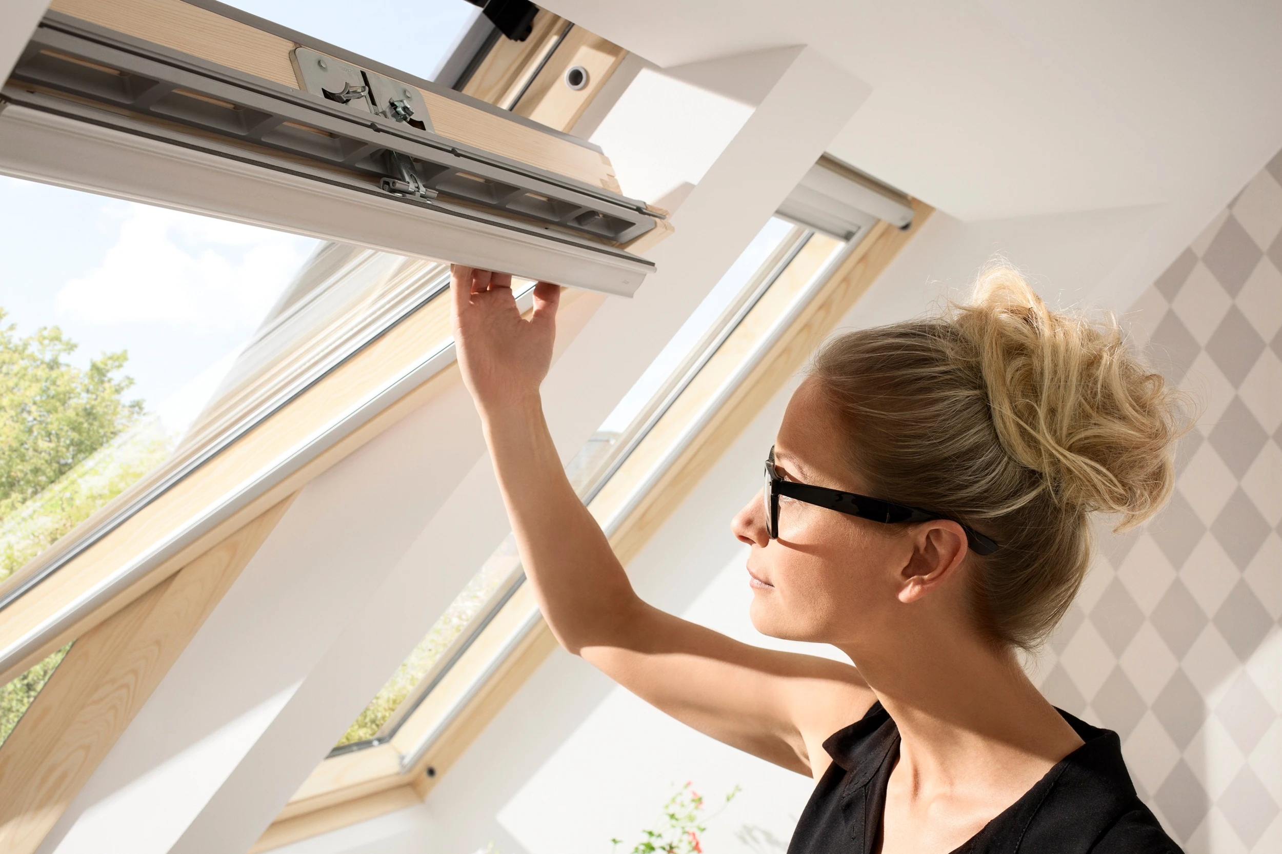 Woman opening a roof window in a bright attic room