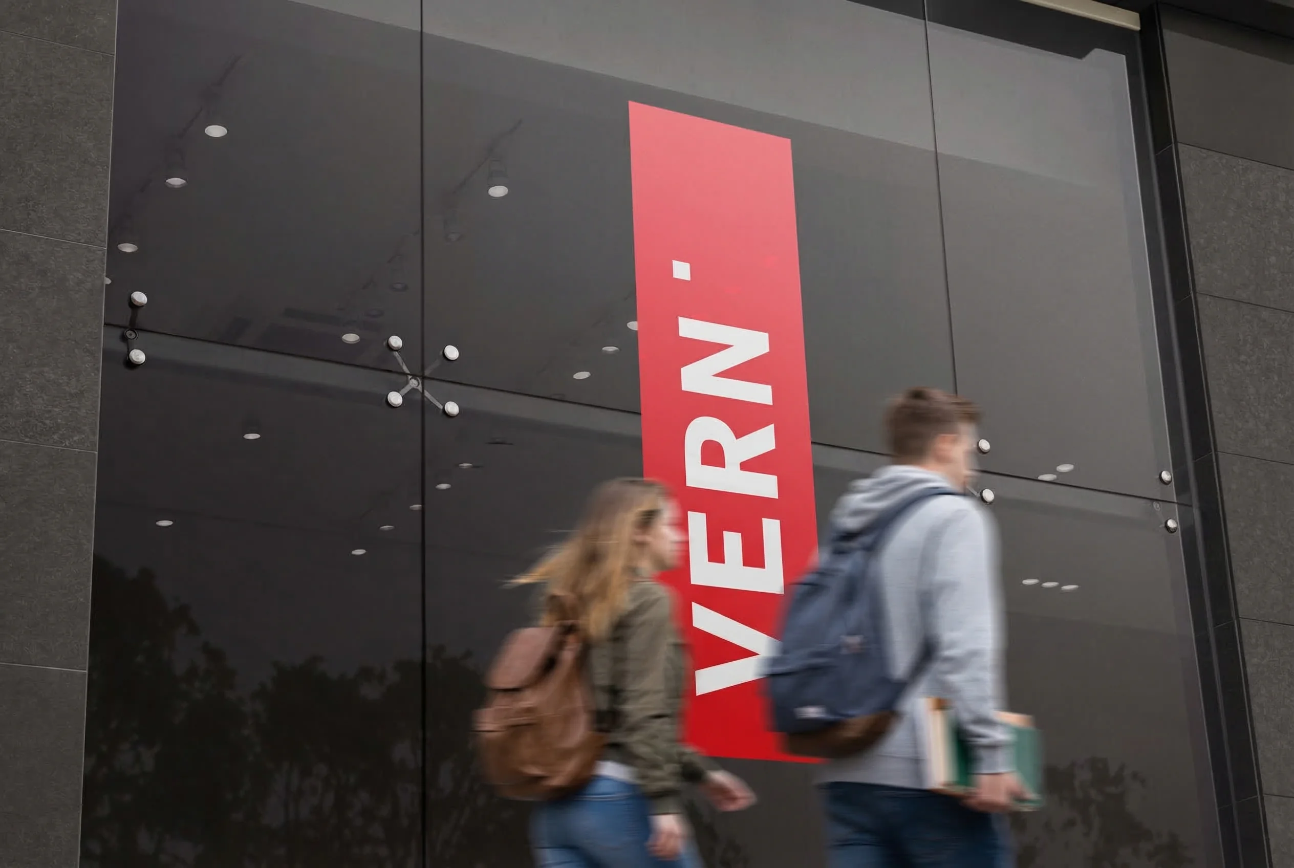 People walking past a red VERN sign on a glass building